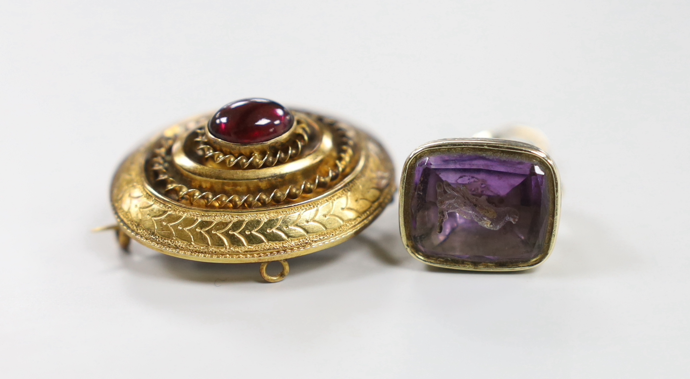 A Victorian yellow metal and single stone cabochon garnet set oval brooch, with glazed back, 29mm and a similar yellow metal overlaid and amethyst set fob seal, the matrix carved with a bird.